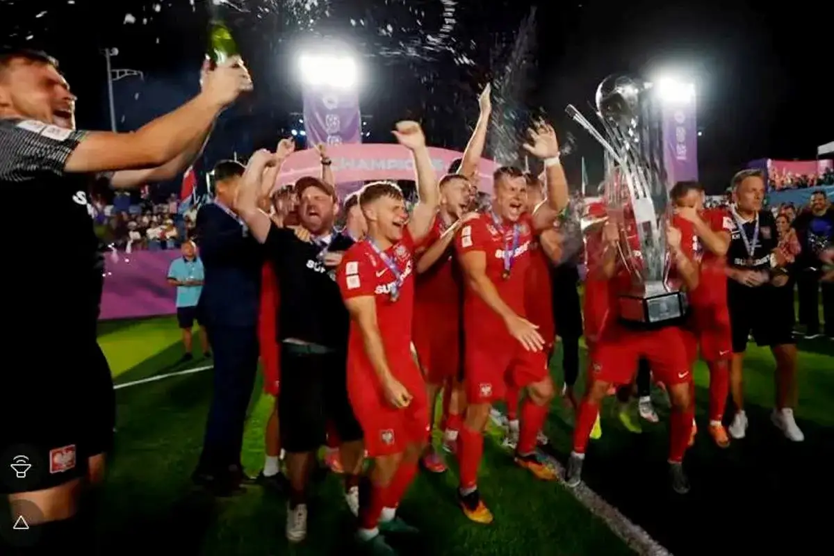 Piłkarze w czerwonych strojach świętują z pucharem i szampanem. Czy Polska kiedyś wygrała mistrzostwa świata? Ta radość sugeruje, że tak!