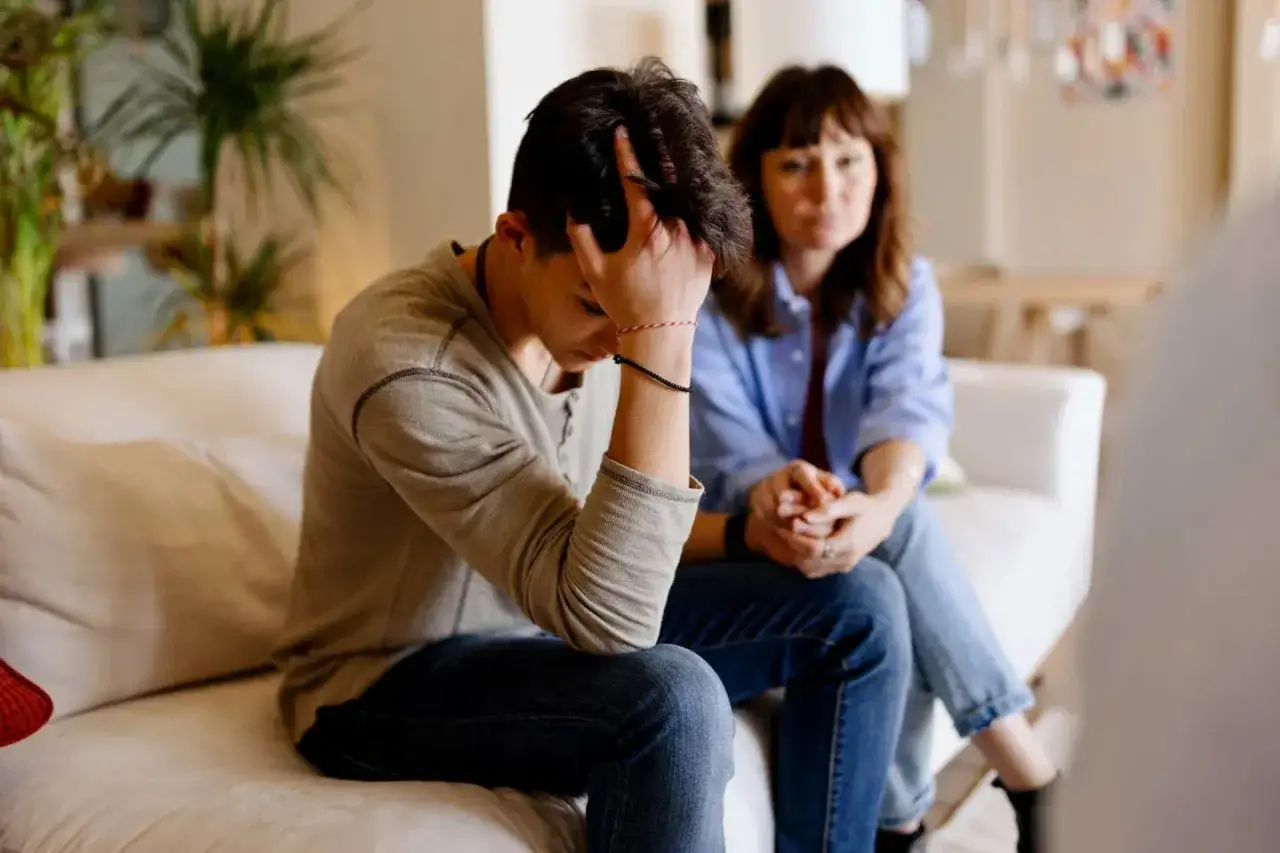 Un adolescent se sent délaissé par son conjoint, la tête dans les mains, tandis que sa mère le regarde avec inquiétude.
