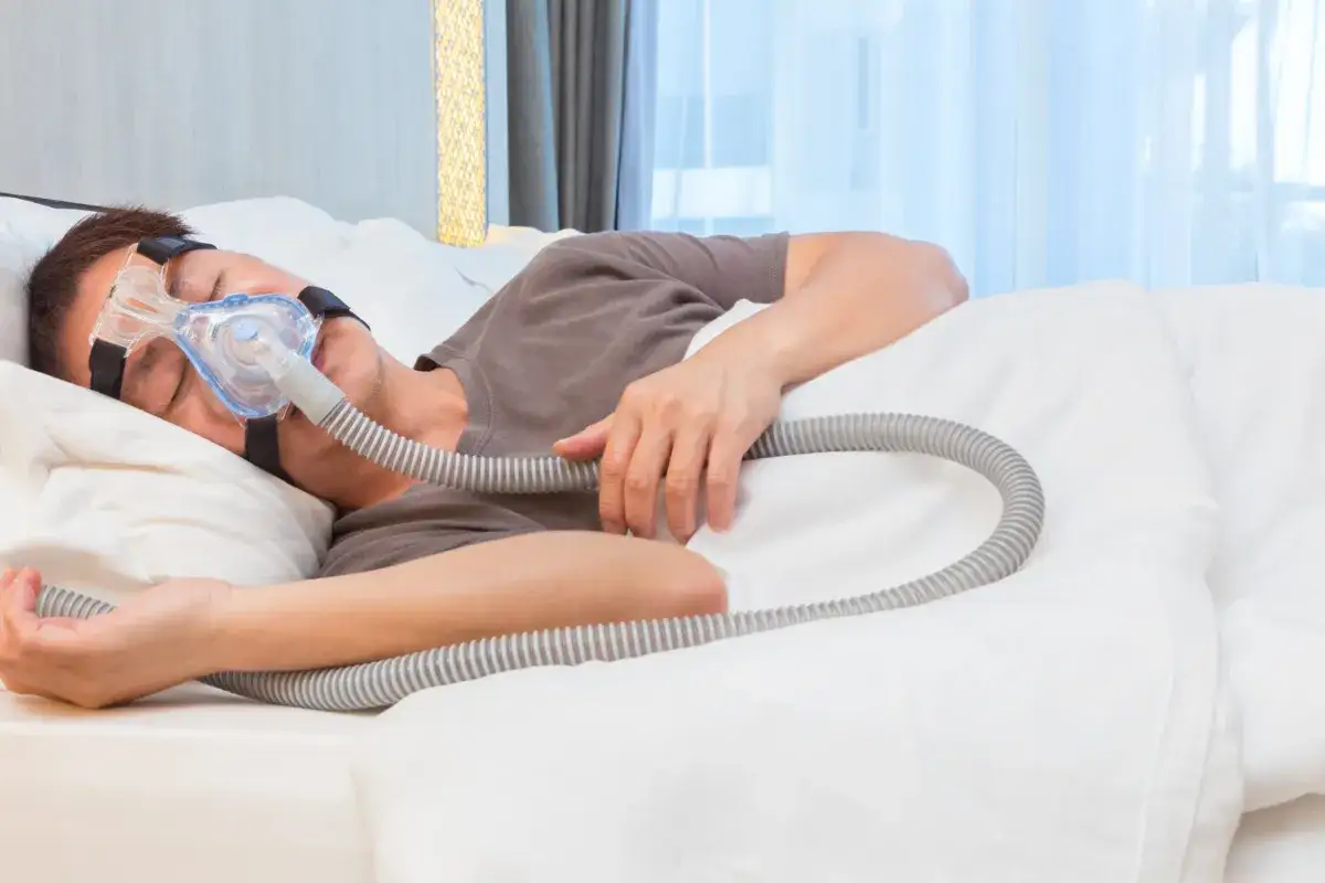 Mężczyzna śpi z maską CPAP, która pomaga w leczeniu bezdechu sennego. To jedno z domowych sposobów na spokojny sen.