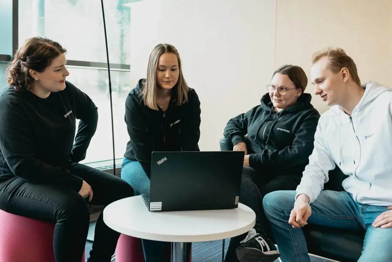 Fyra kollegor sitter runt ett bord och tittar p&aring; en laptop. De verkar diskutera och samarbeta, vilket visar hur man kan **utveckla medarbetare** genom gemensamt l&auml;rande.