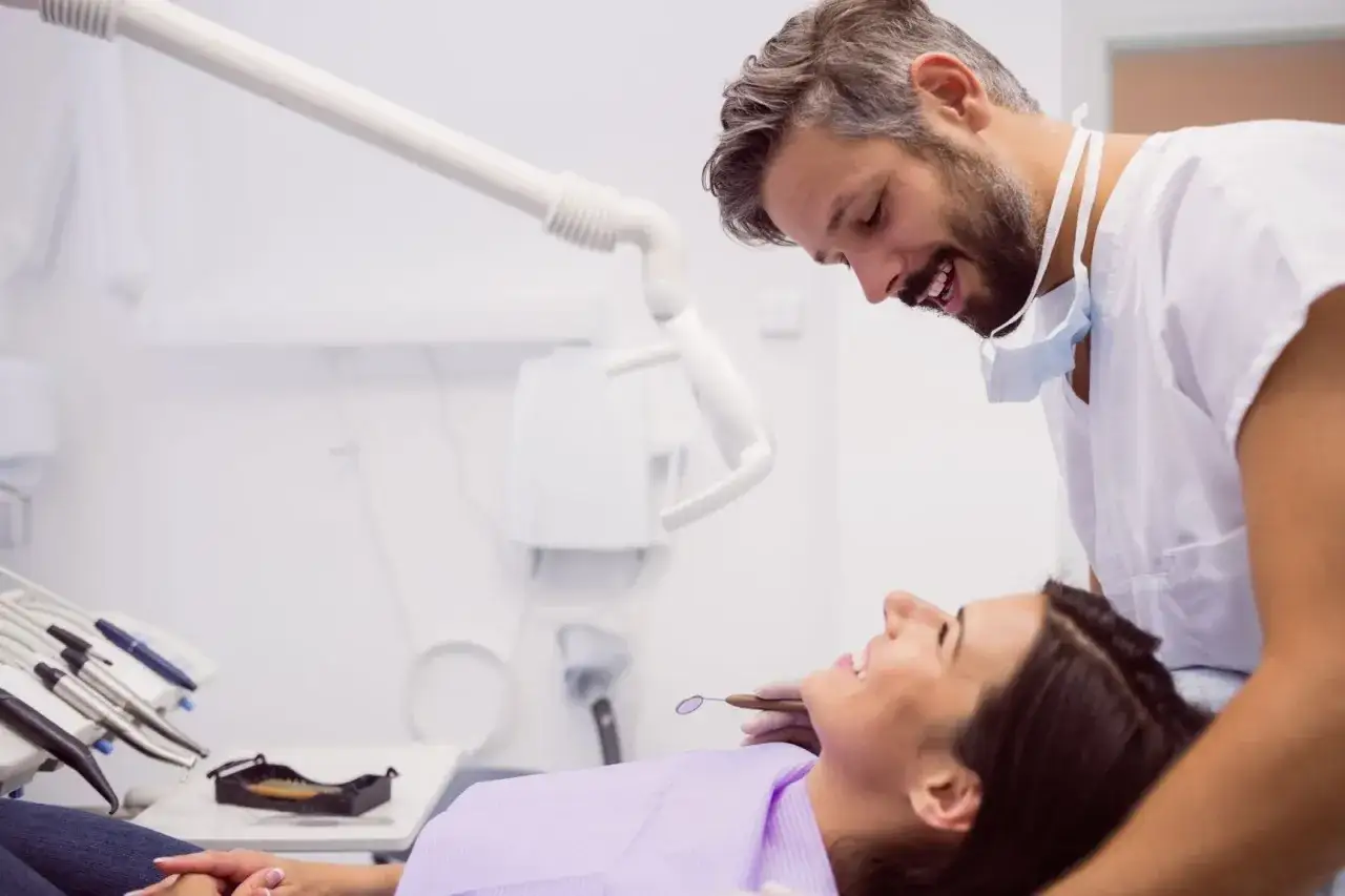 Dentista sonriente revisa la boca de una paciente, indicando una consulta para fluorización dental en adultos.