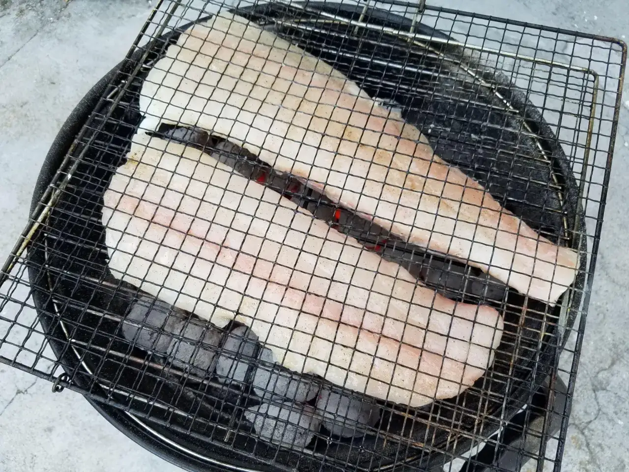 Deux filets de cabillaud au barbecue, prêts à être grillés sur des braises ardentes.