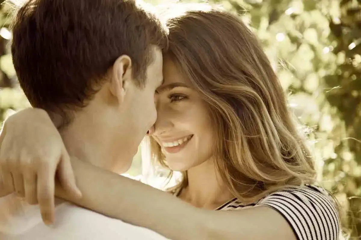 Un jeune couple s'embrasse tendrement, leurs fronts se touchant. Un sourire radieux illumine le visage de la jeune femme, annonçant le début d'une histoire d'amour.