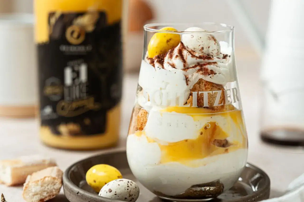 Cremiges Tiramisu ohne Alkohol im Glas, geschichtet mit Löffelbiskuits, Mascarponecreme und Fruchtpüree. Dekoriert mit Kakaopulver und Schokoladeneiern.