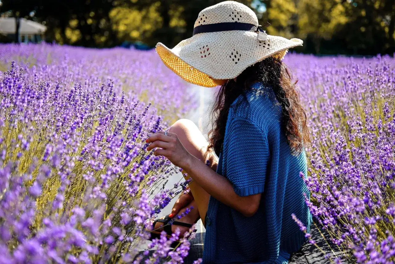 Mujer con sombrero de paja en campo de lavanda, disfrutando de la belleza y los cuidados de estas flores.