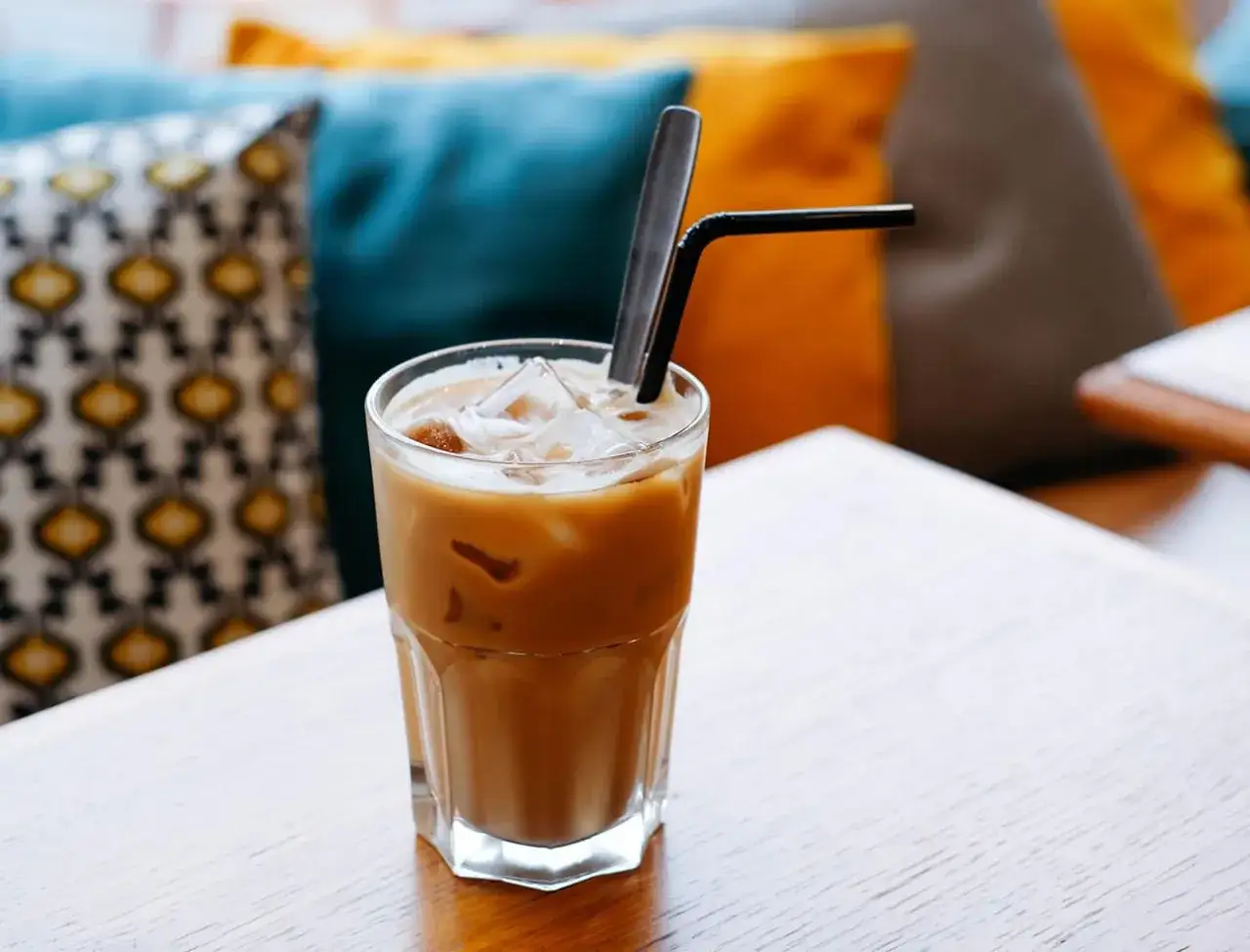 Un bicchiere di caff&egrave; freddo, con ghiaccio e cannuccia, su un tavolo di legno. Perfetto per una pausa estiva.