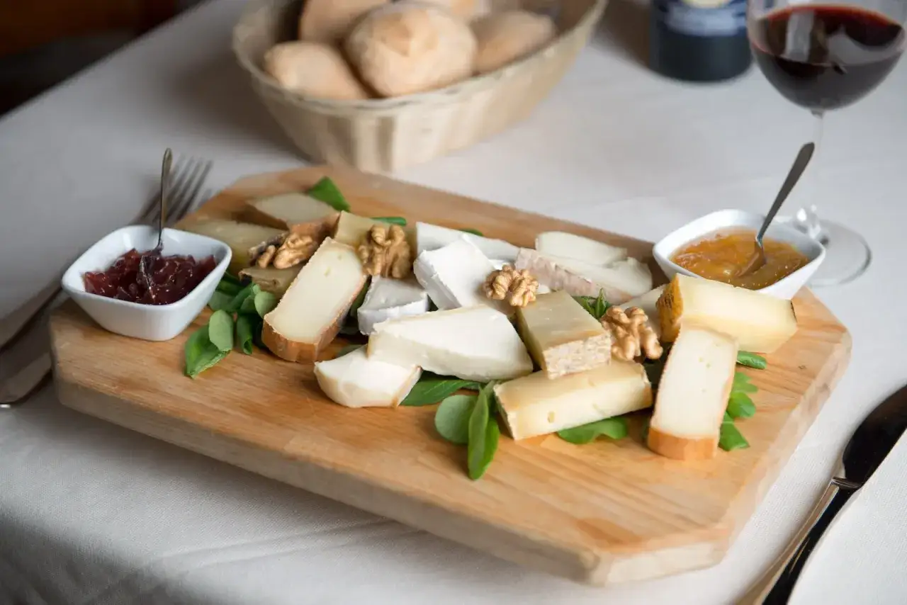 Tagliere di formaggi pasta semidura, noci e marmellate, accompagnato da pane e vino rosso.