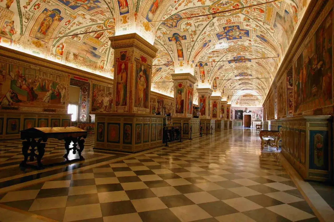 Wnętrze Galerii Map w Watykanie, części największego muzeum świata, z malowanymi sklepieniami i posadzką w szachownicę.