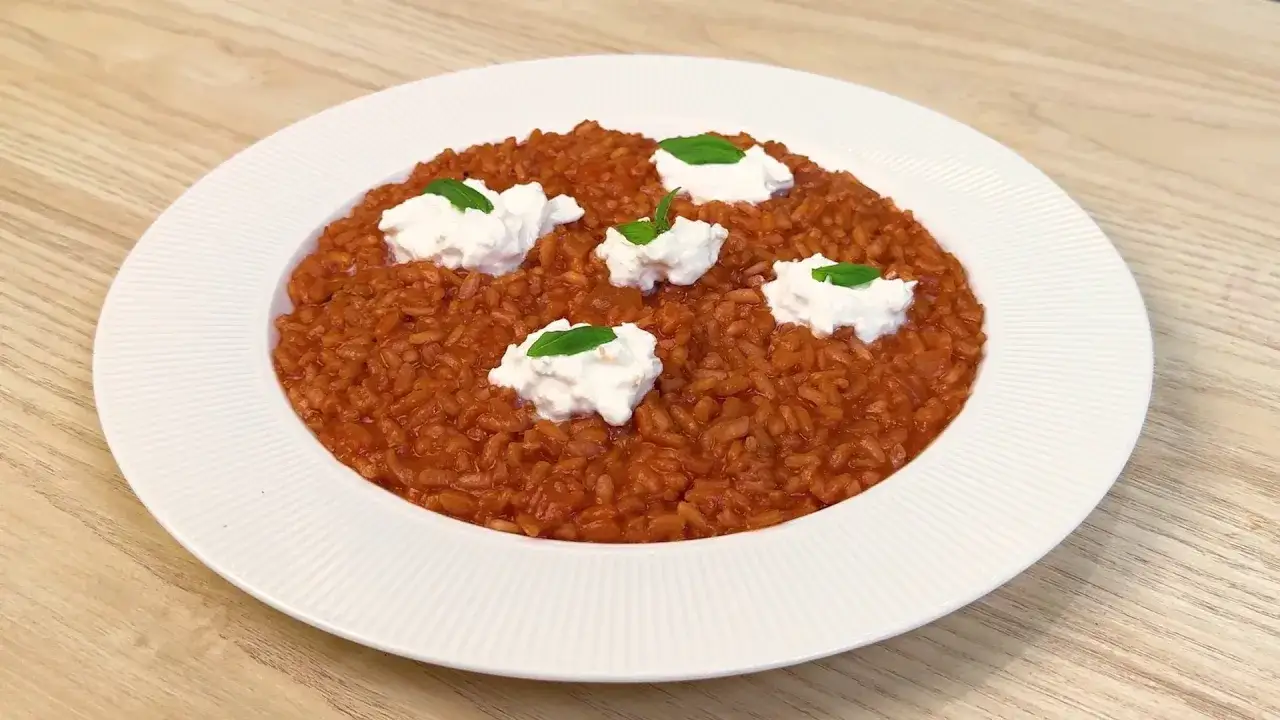 Un cremoso risotto al pomodoro, guarnito con ciuffi di ricotta fresca e foglie di basilico, pronto per essere gustato.
