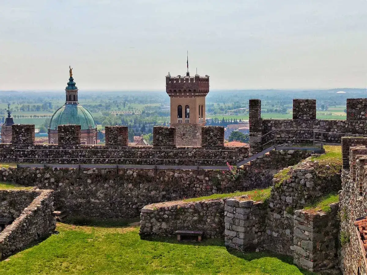 Rovine del castello di Lonato sul Garda con una torre merlata e una cupola verde in lontananza.