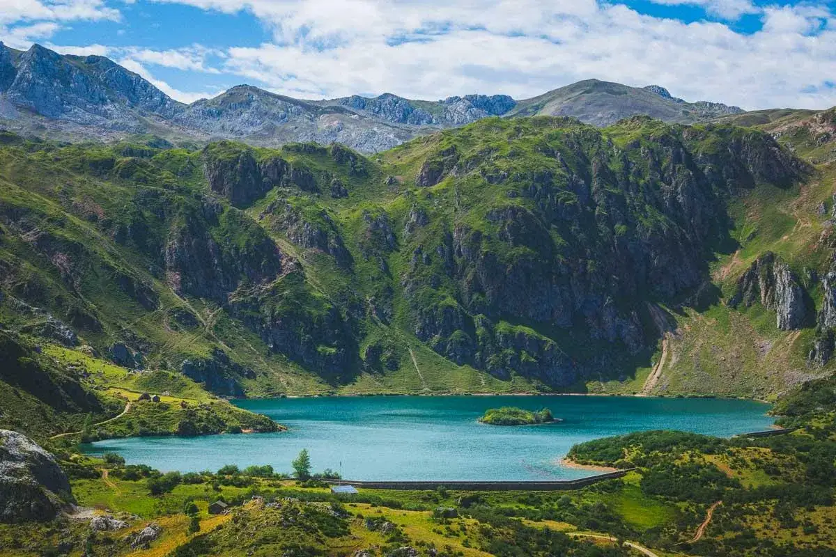 Paisaje monta&ntilde;oso con un lago turquesa en Somiedo. Senderos serpentean por las laderas verdes, invitando a explorar las rutas en Somiedo.