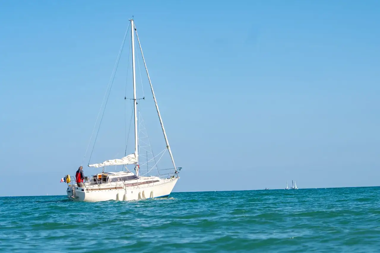 Un voilier blanc navigue sur une mer bleue près du port de l'Île d'Oléron. Le ciel est clair et dégagé.
