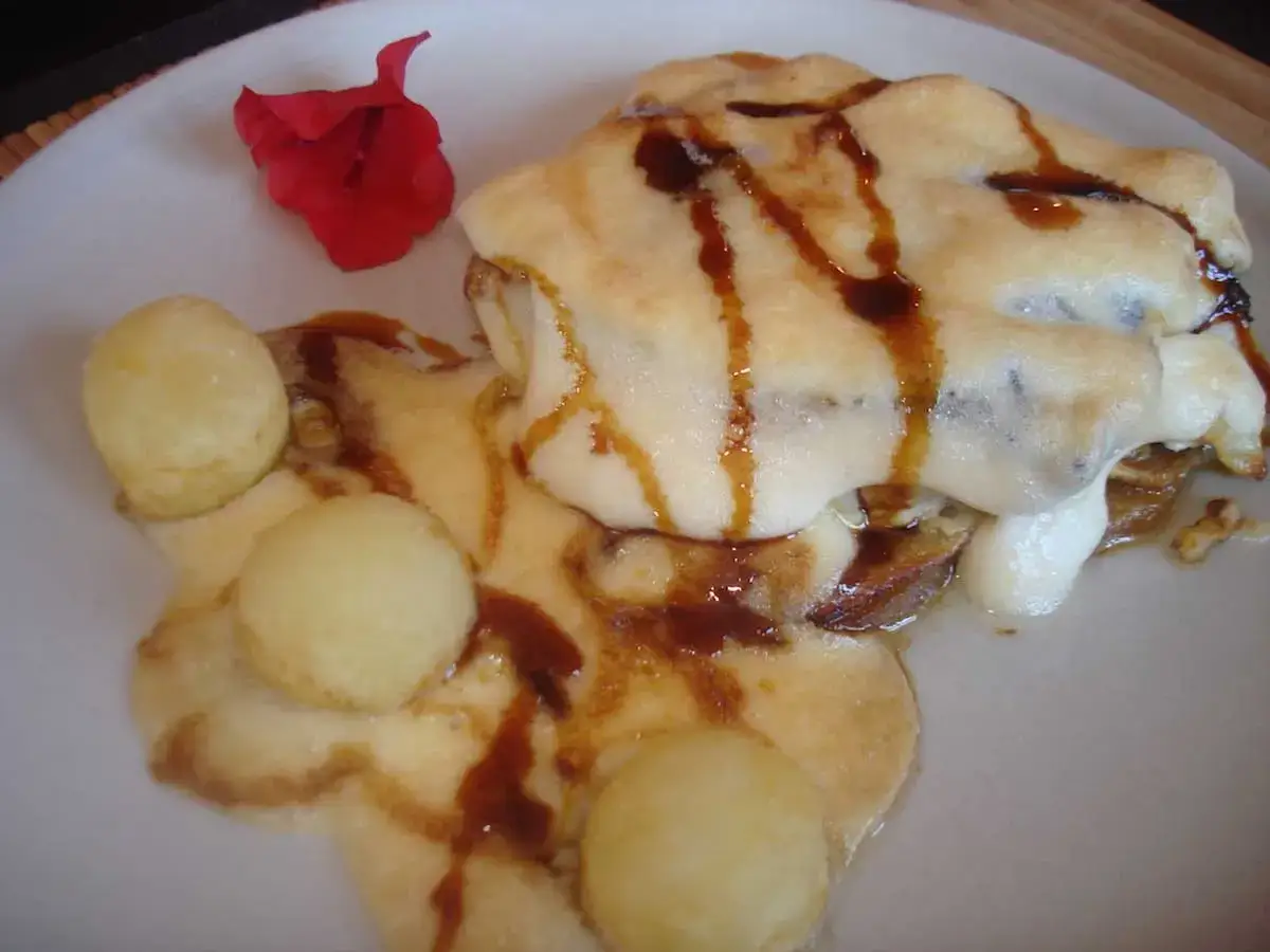 Delicioso bacalao gratinado con alioli, acompañado de unas bolitas doradas y un toque de salsa oscura.