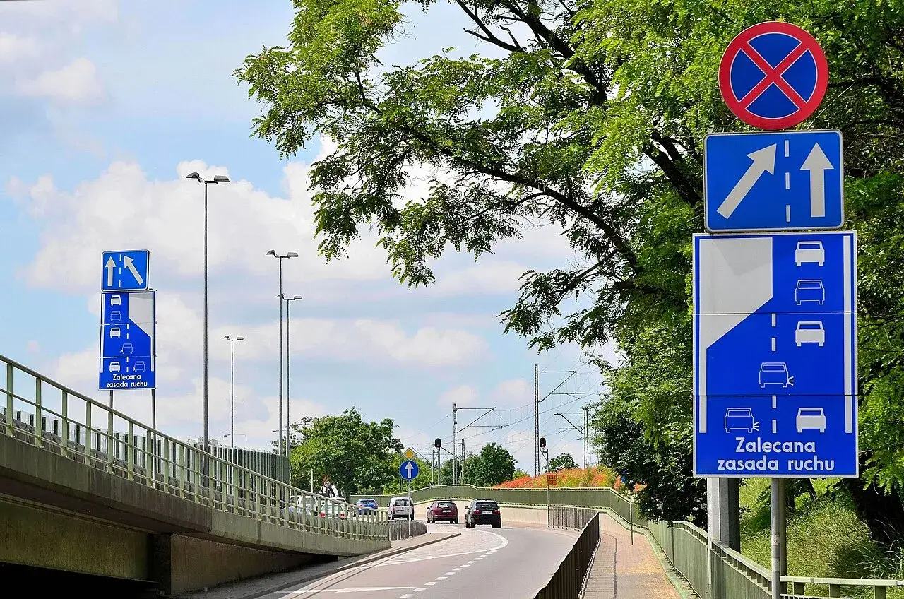 Znaki drogowe wskazują zalecaną zasadę ruchu: jazda na suwak. Samochody zbliżają się do zwężenia drogi.