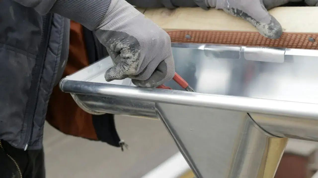 Hand mit Handschuh dichtet mit Werkzeug eine Dachrinne ab.