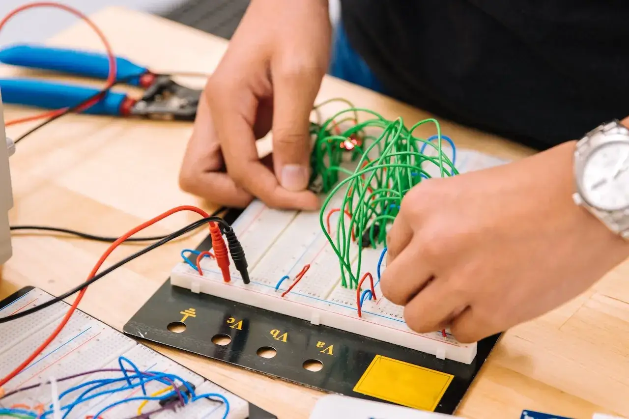 Mani che assemblano circuiti su breadboard, un'attività che fa riflettere su quanto guadagna un meccanico industriale.