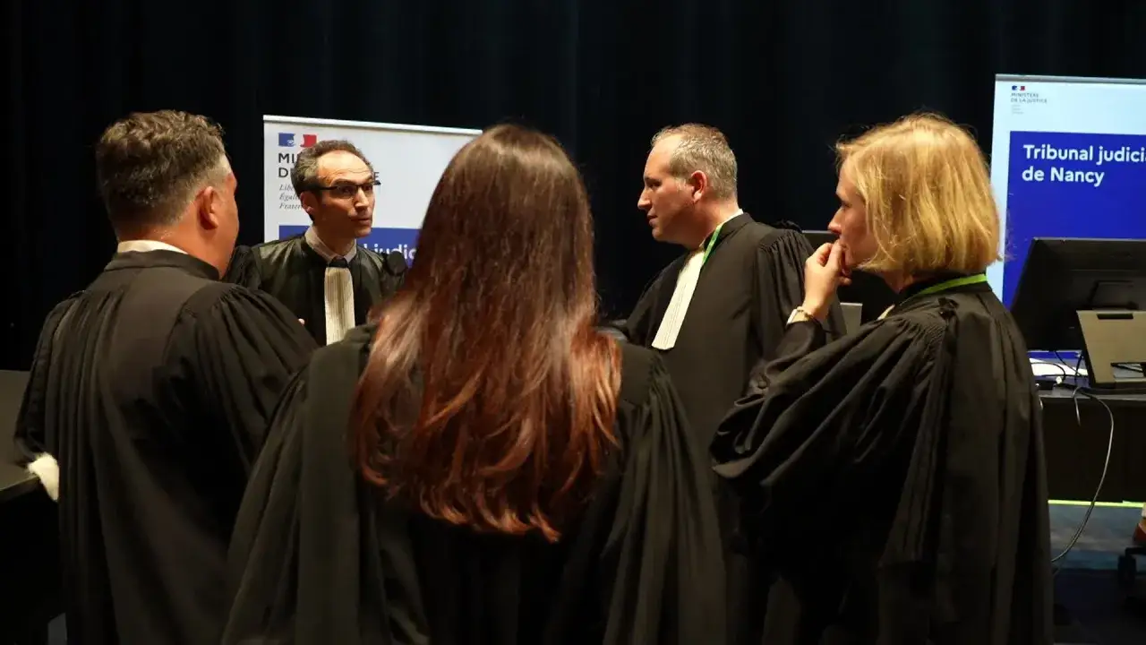Des avocats en robe discutent. L'un d'eux semble préoccupé, peut-être par une affaire de **peine escroquerie**.