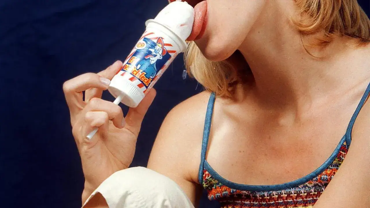 Ein Mini Milk Eis im 90er-Jahre-Design, das von einer Frau genossen wird.