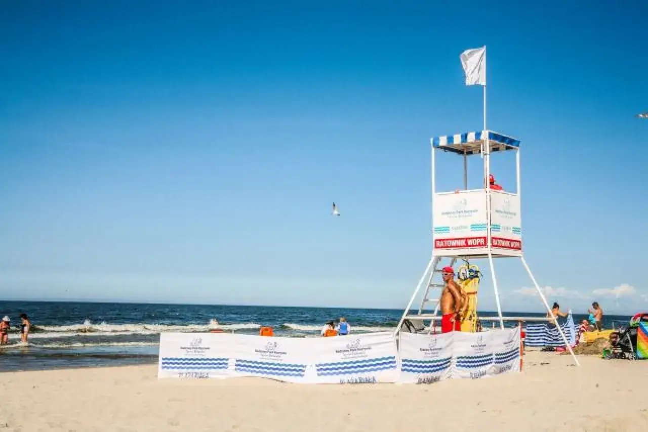 Ratownik na plaży, biała flaga co oznacza bezpieczną kąpiel. Słońce, morze i wypoczywający ludzie.