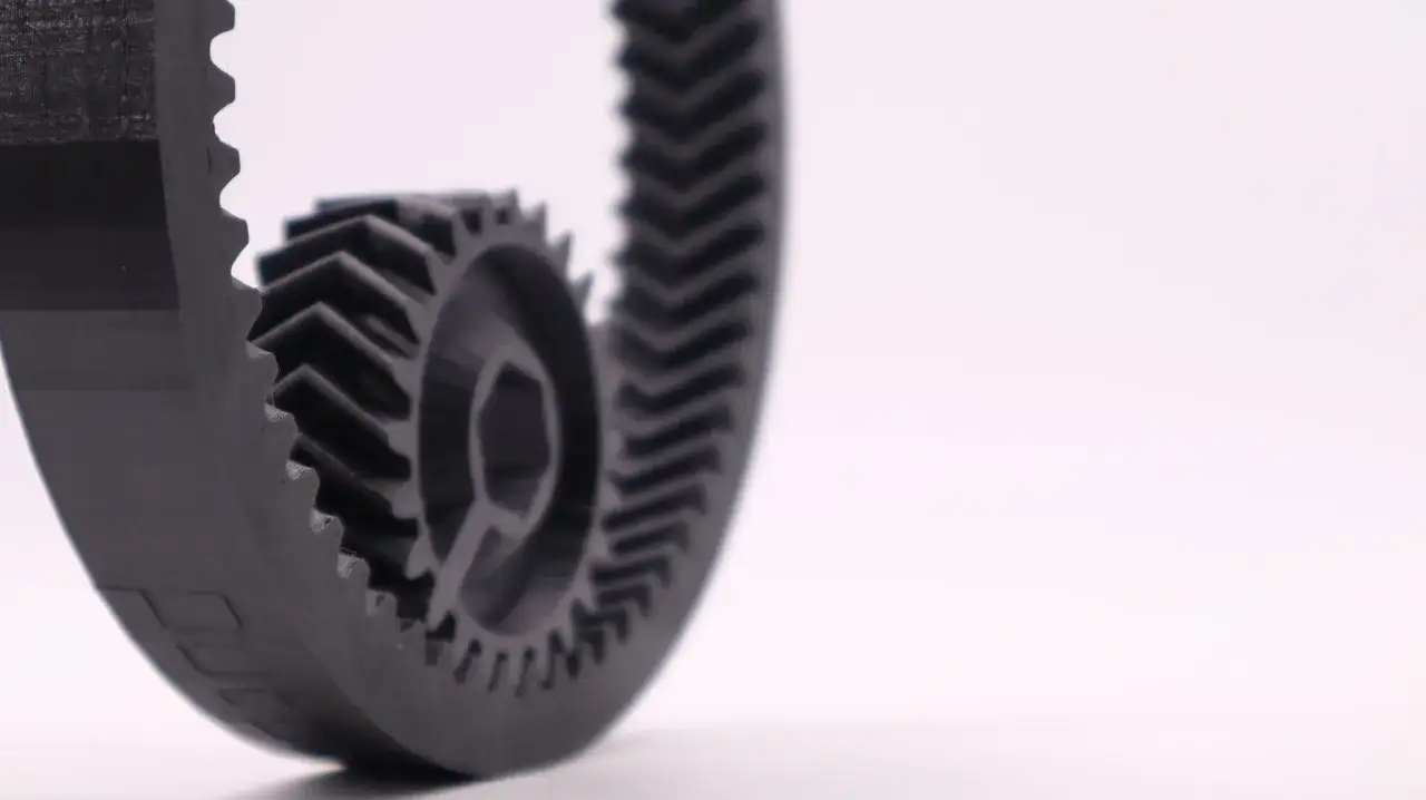 A close-up of a black, gear-like object, showcasing the intricate details achieved through carbon fiber 3D printing.