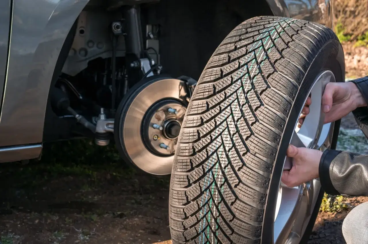 Cambio gomme: un nuovo pneumatico con disegno a freccia rotazione pronto per essere montato sull'auto.
