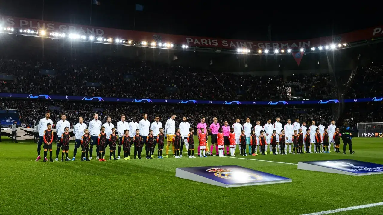 Piłkarze i dzieci stoją na murawie stadionu, słuchając hymnu Ligi Mistrzów.