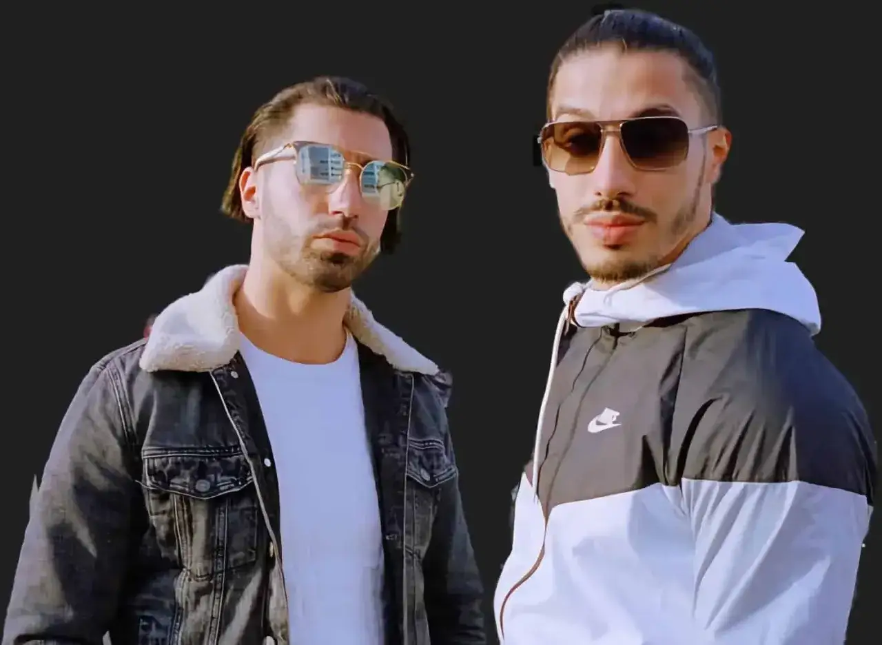 Dwóch mężczyzn w okularach przeciwsłonecznych, gotowych na podbój sceny francuskiego rapu. Jeden w jeansowej kurtce z kołnierzem, drugi w sportowej bluzie Nike.