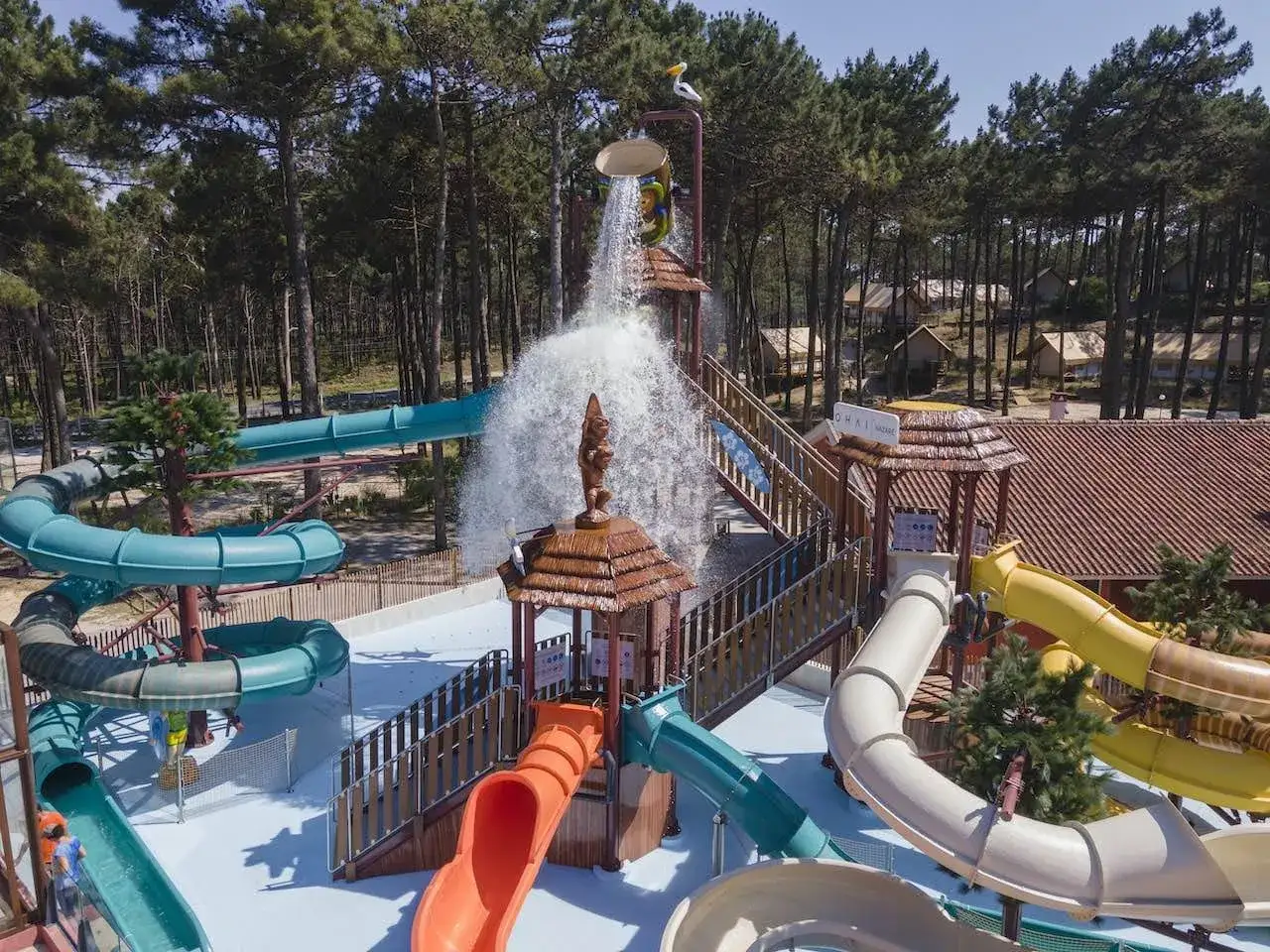 Parque acuático con toboganes coloridos y una cascada gigante, rodeado de pinos. Ideal para unas vacaciones de camping en Lisboa.