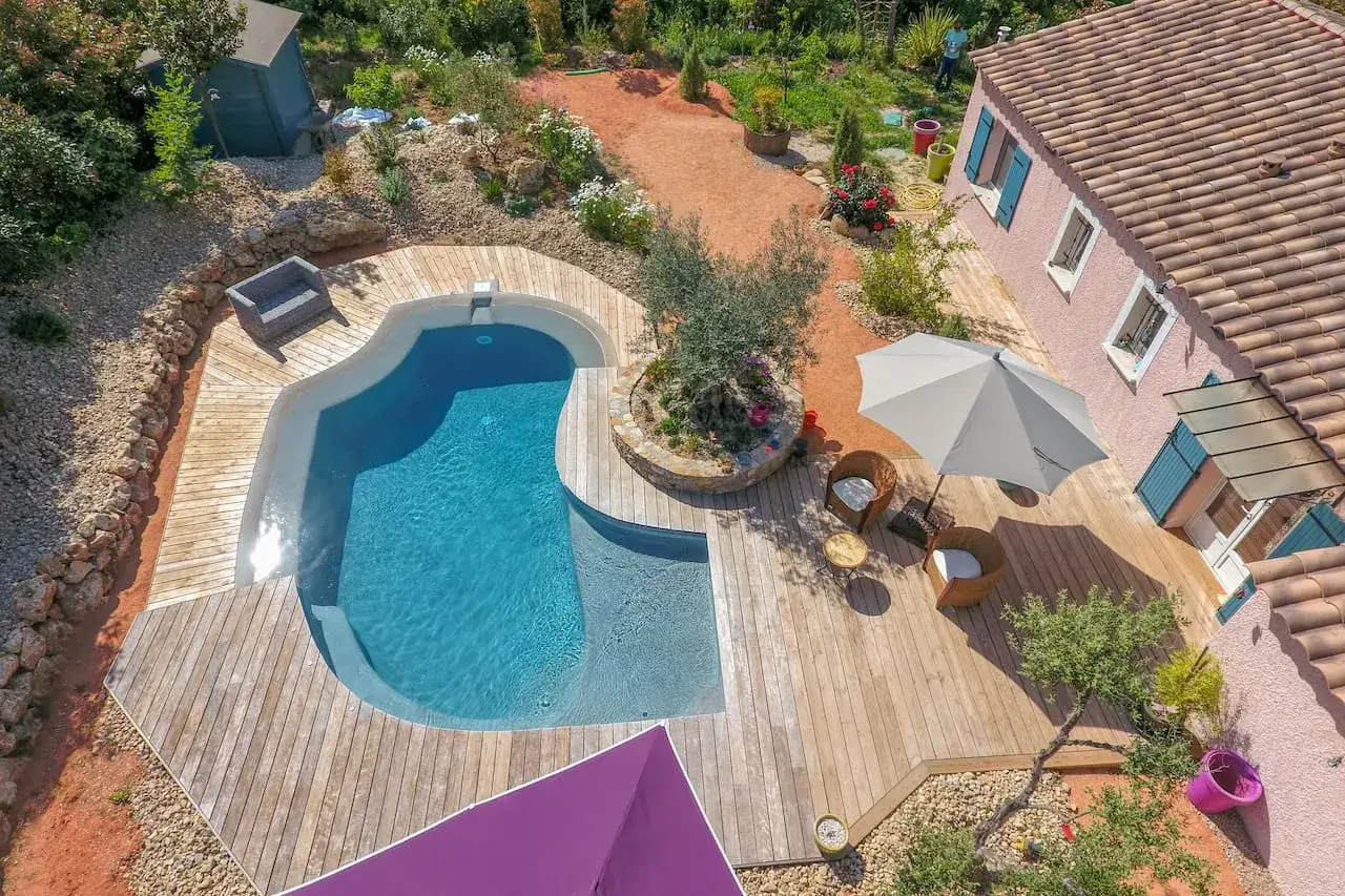 Belle terrasse bois autour d'une piscine sans margelle, avec mobilier de jardin et parasol. Un coin paisible pour se d&eacute;tendre.