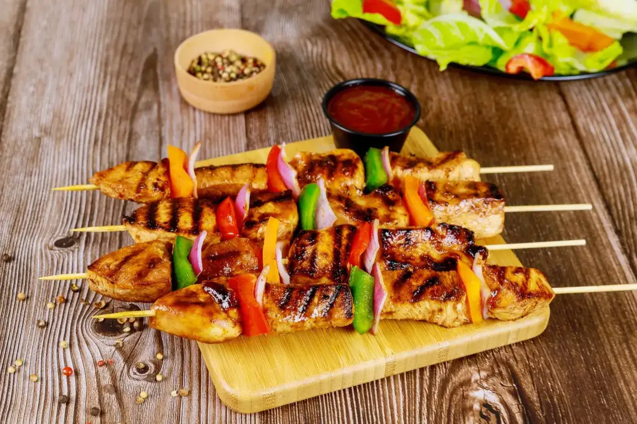 Brochettes de poulet grillées, colorées de poivrons et d'oignons, servies sur une planche en bois avec une sauce barbecue.
