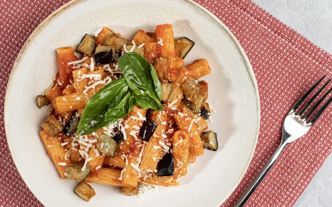 Piatto di pasta con melanzane in bianco, condita con pomodoro e basilico fresco, spolverata di formaggio grattugiato.