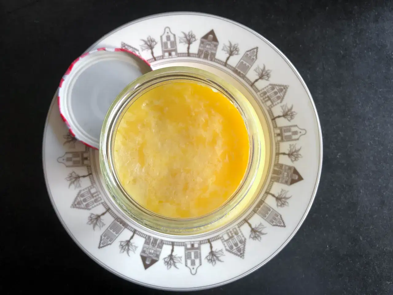 Un pot de beurre clarifi&eacute;, un ingr&eacute;dient essentiel pour la cuisine, repose sur une assiette d&eacute;cor&eacute;e de maisons hollandaises.