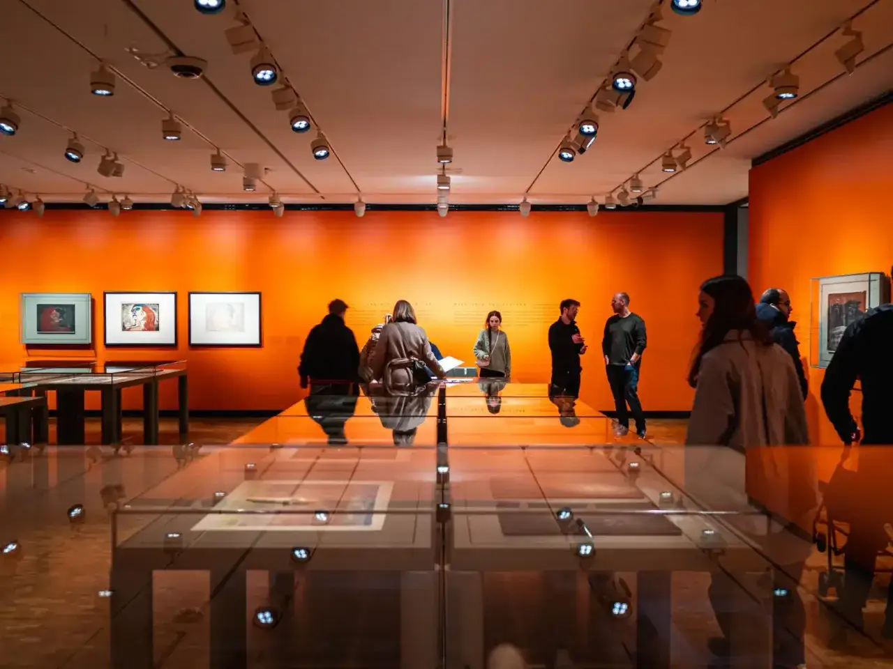 Wystawa w Muzeum Narodowym w Oslo. Zwiedzający oglądają obrazy na pomarańczowej ścianie.