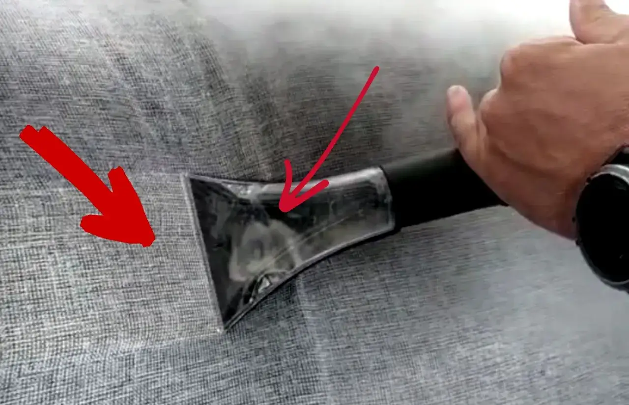 Mit Rasierschaum Polster reinigen: Ein Handgriff mit Aufsatz saugt Schmutz von grauem Stoff.