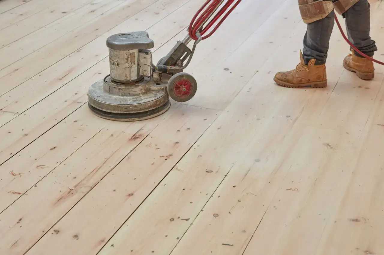 Un trabajador pule un suelo de madera con una máquina. El parquet se puede acuchillar varias veces para renovarlo.
