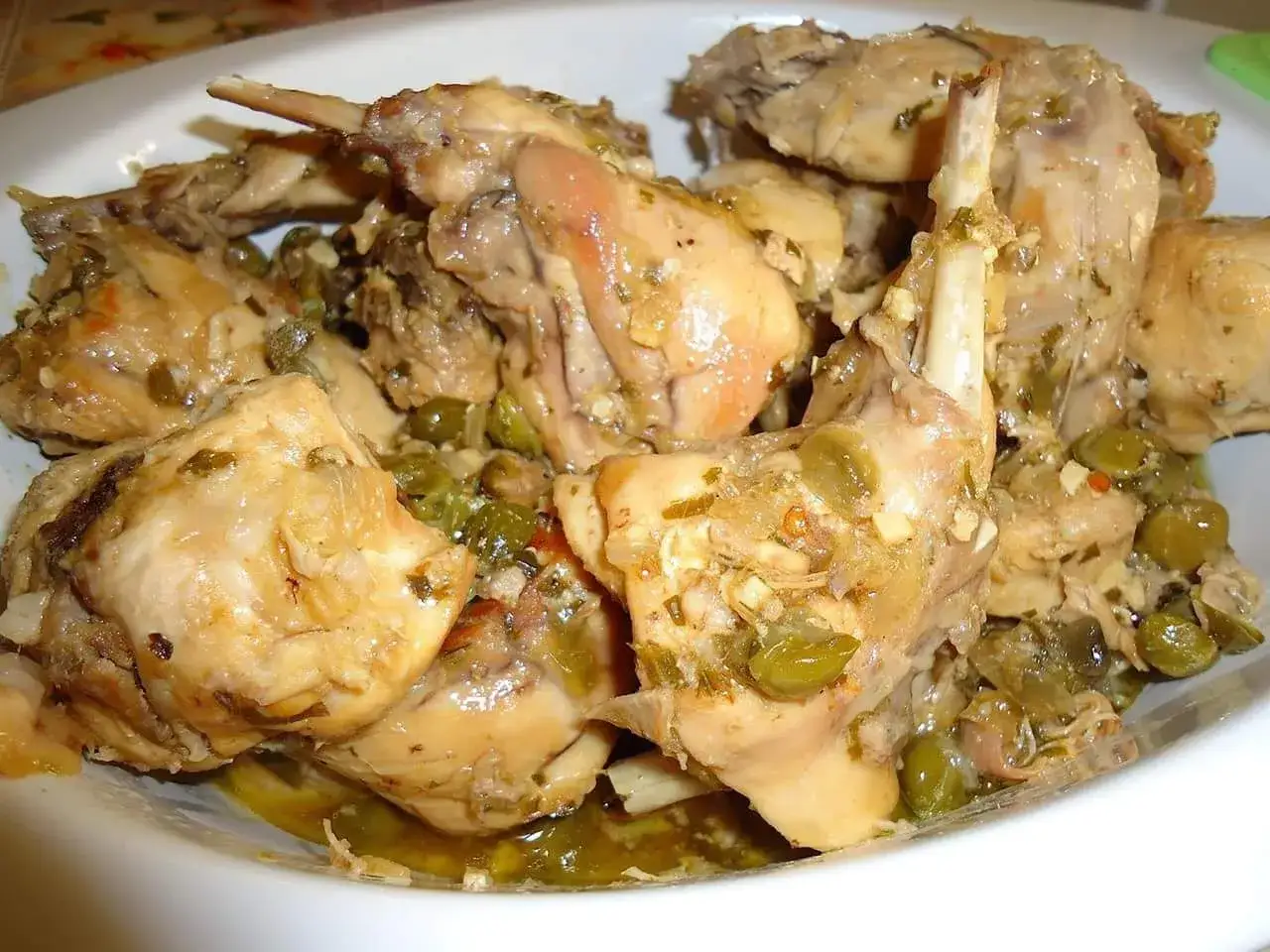 Un saporito coniglio alla cacciatora in bianco, con olive verdi e erbe aromatiche, pronto per essere gustato.