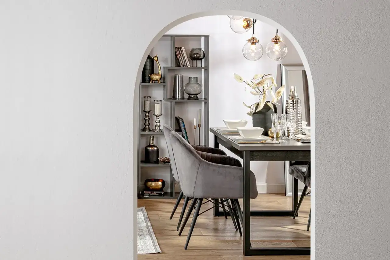 Elegancki łuk w salonie inspiracje: szare krzesła, stół z zastawą, półki z dekoracjami i stylowe lampy.