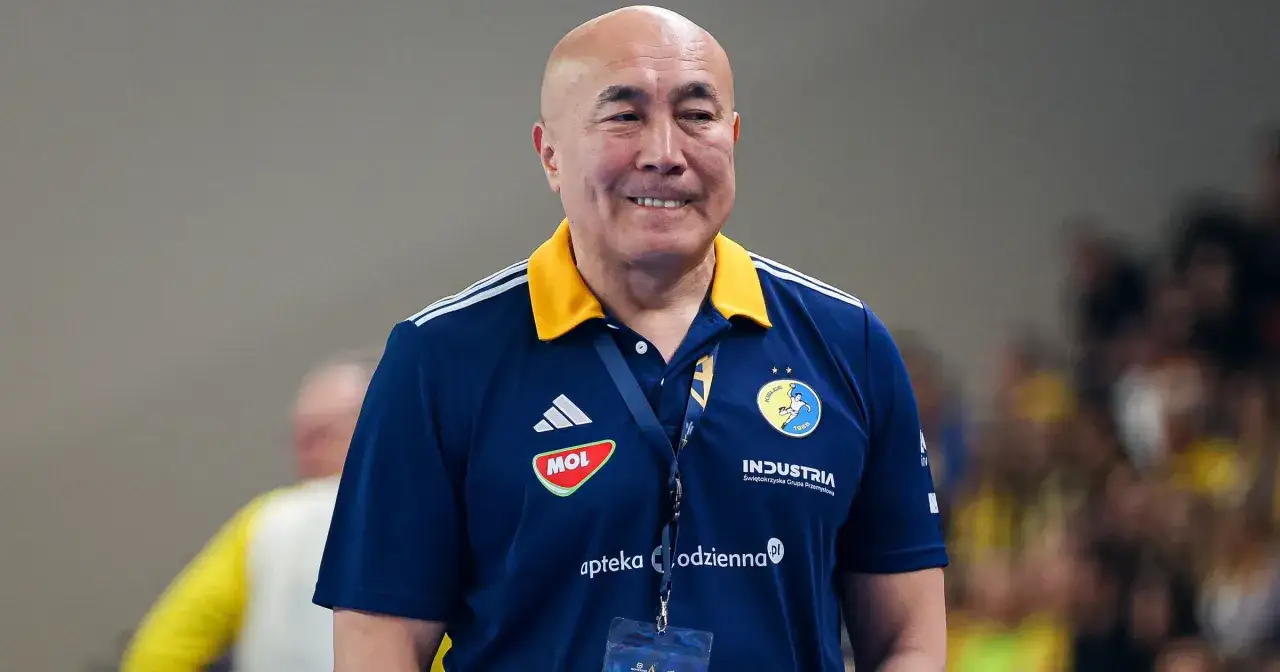 Uśmiechnięty trener Vive Kielce w granatowej koszulce z ż&oacute;łtym kołnierzem, z logo klubu na piersi.
