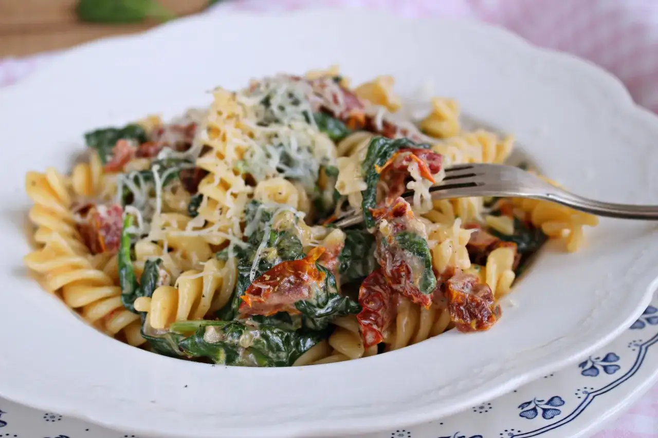 Fusilli z szpinakiem i suszonymi pomidorami, posypane parmezanem. Widok z bliska na talerz pełen aromatycznego makaronu.