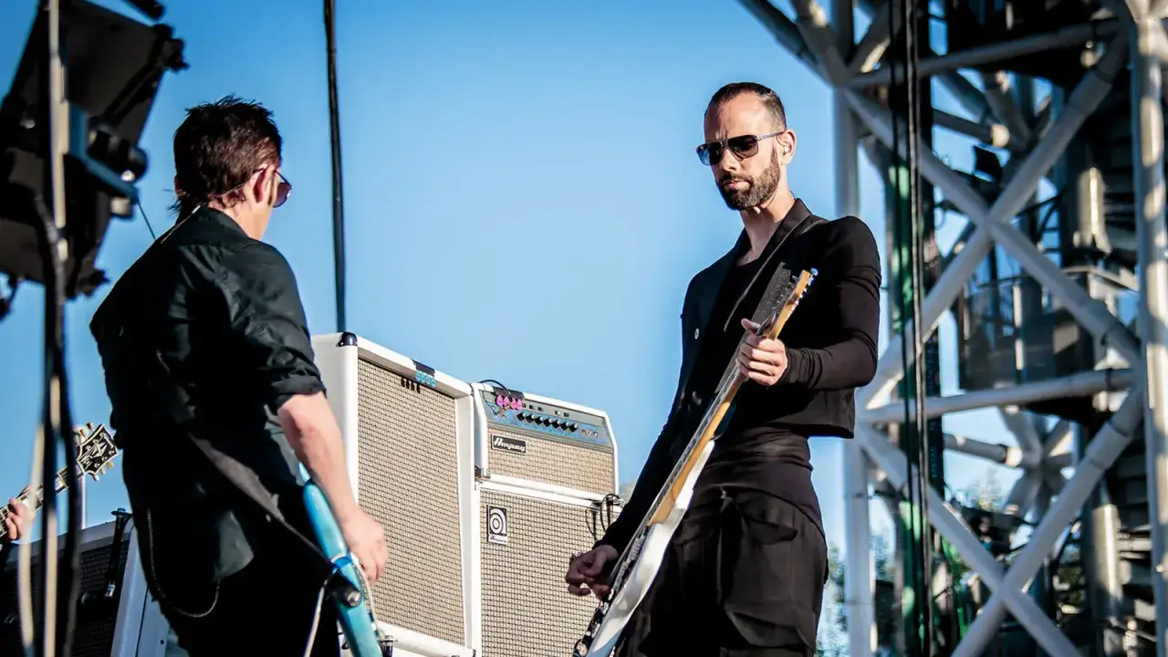 Zespół Placebo na scenie. Brian Molko w okularach przeciwsłonecznych gra na gitarze.