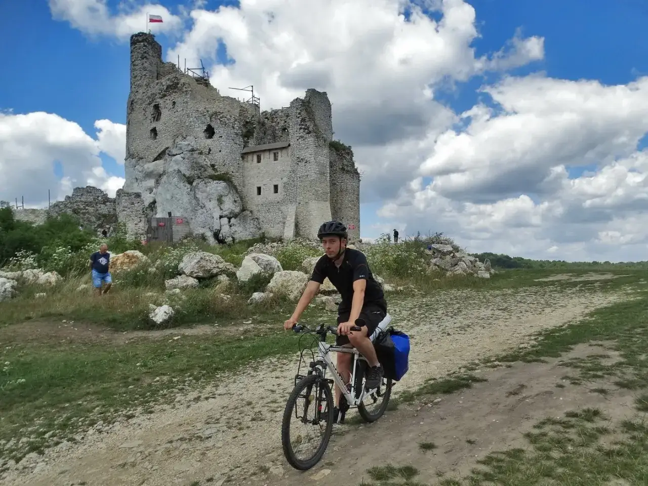 Młody rowerzysta przemierza szlak na Jurze Krakowsko-Częstochowskiej, mijając ruiny zamku na skale.