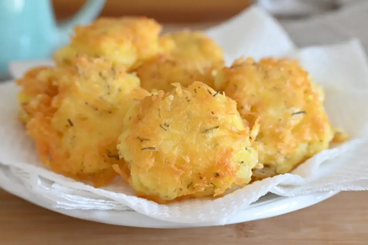 Frittelle di patate dorate e croccanti, condite con erbe aromatiche, servite su un piatto bianco con tovaglioli di carta.