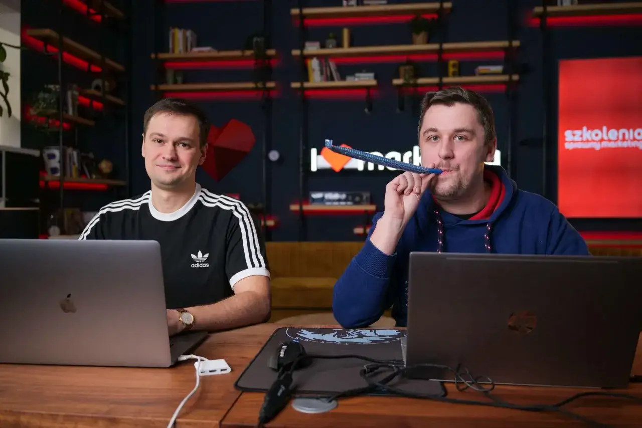 Dw&oacute;ch mężczyzn przy laptopach, jeden z nich dmucha w gwizdek. Uczą się pozycjonowania stron.