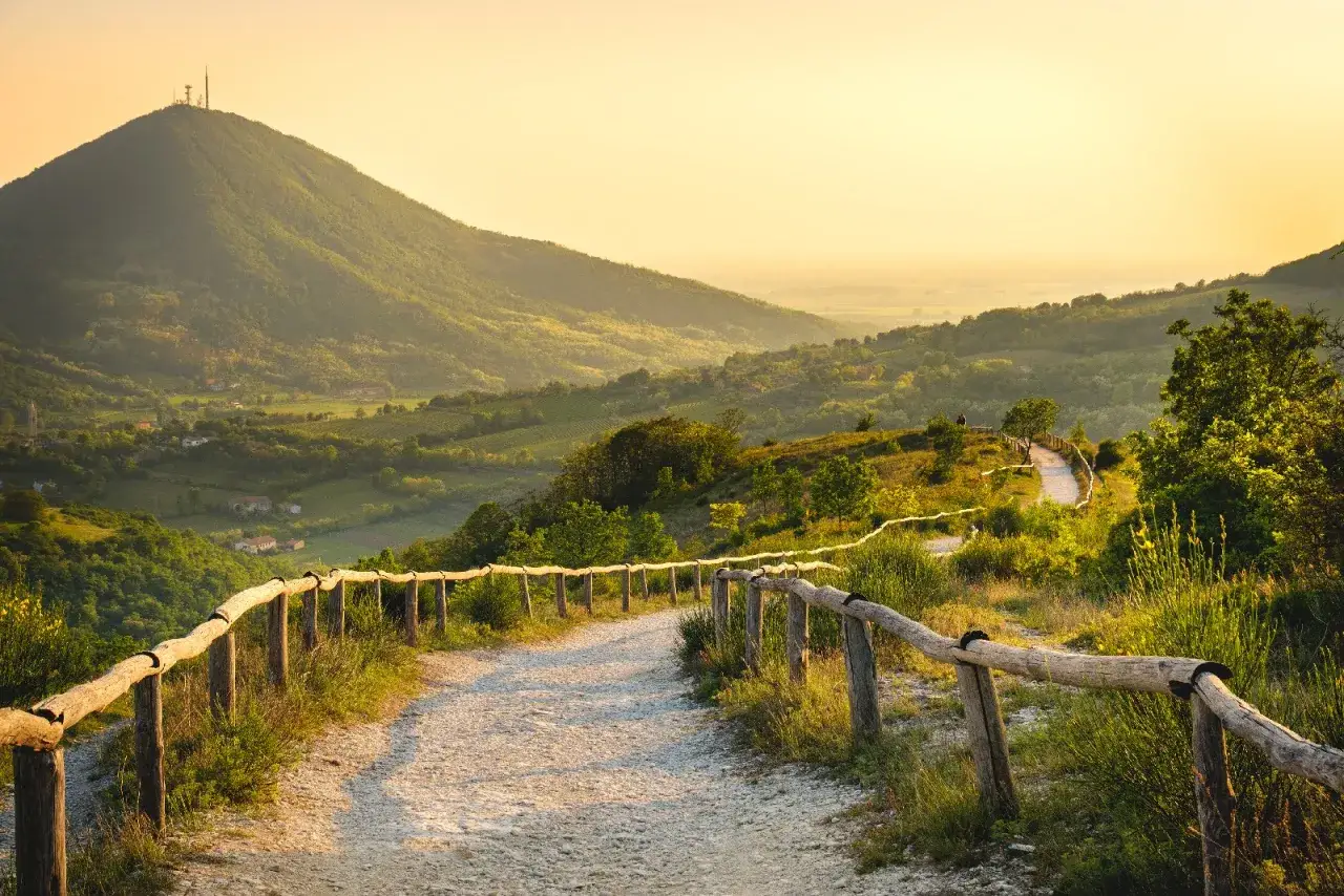 Sentiero sul pianoro del Mottolone al tramonto, con vista su colline verdi e un cielo dorato.