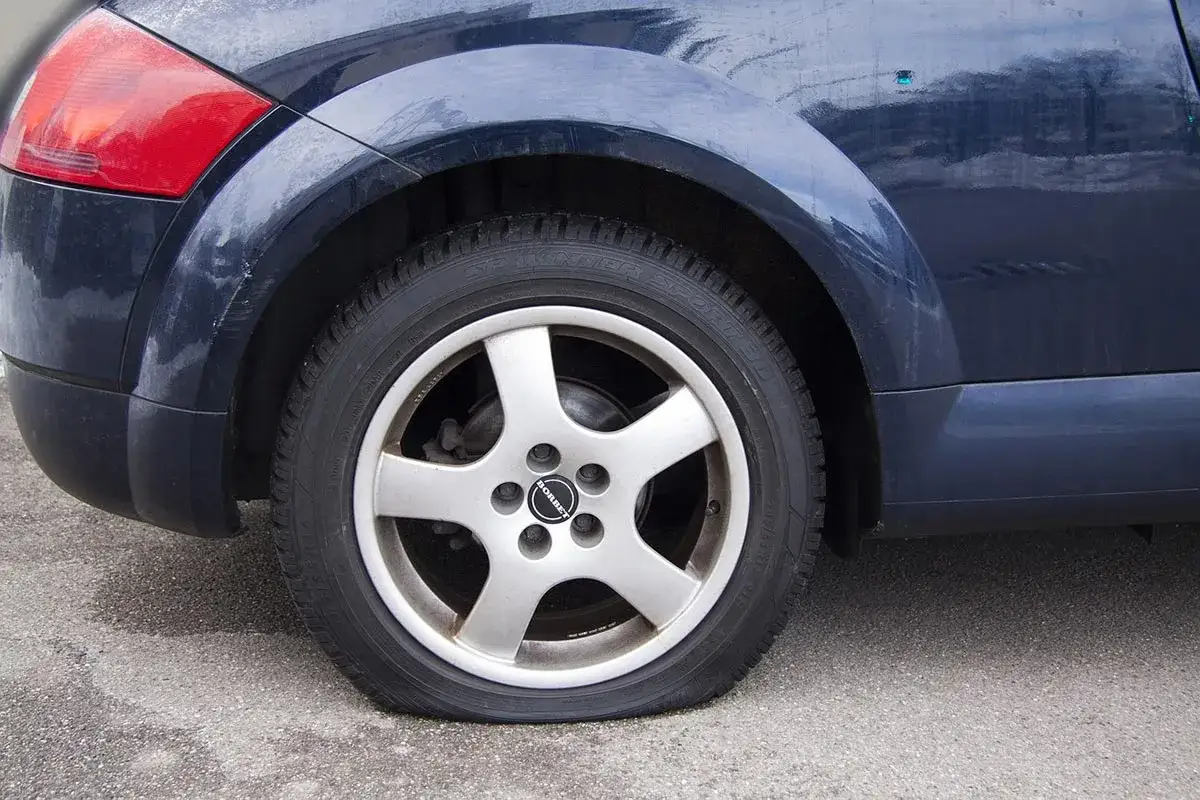 Ruota sgonfia di un'auto blu scuro. Il pneumatico &egrave; completamente a terra, appoggiato sul cerchione.