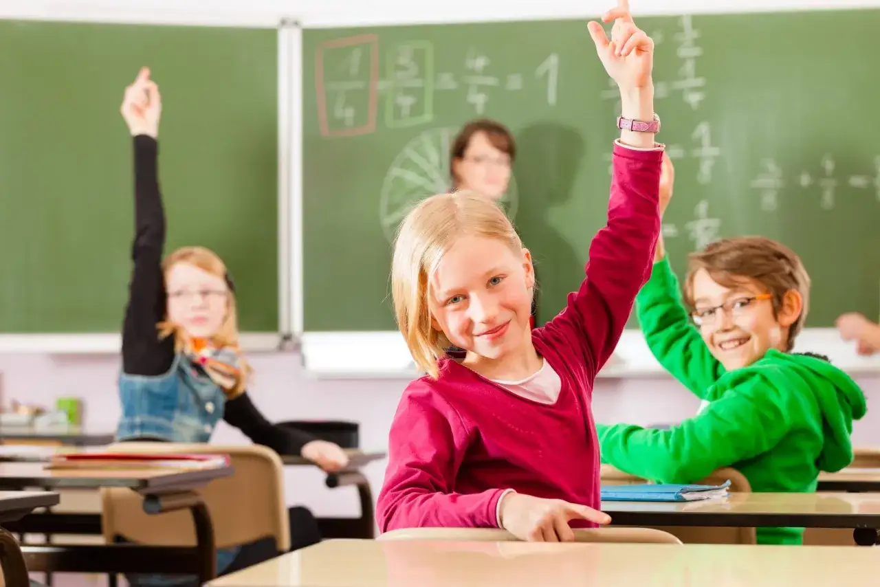 Bambini in classe alzano la mano, entusiasti di rispondere a domande di matematica. Esempi di problem solving in azione.