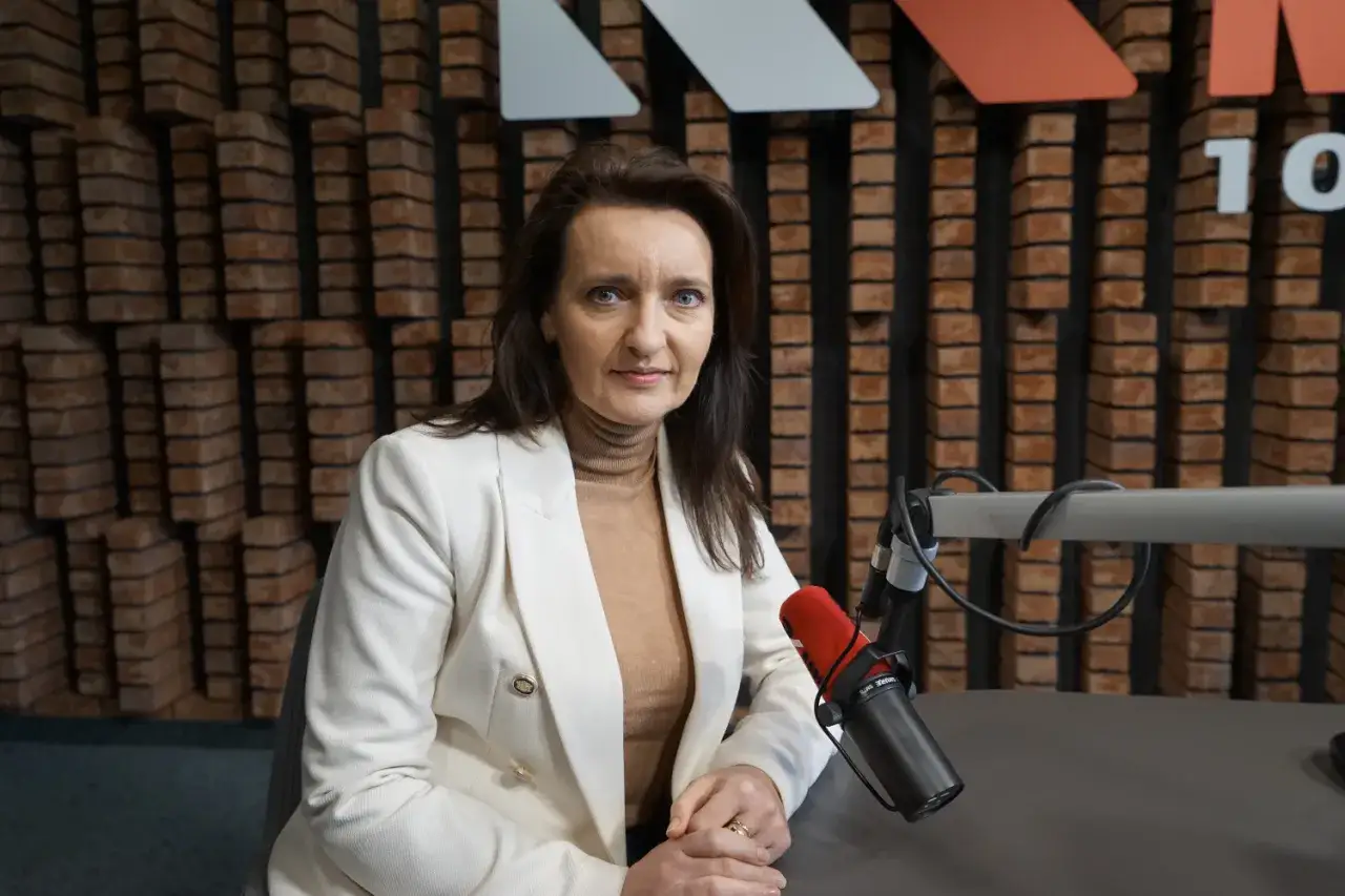Marzena Okła-Dreszner w białej marynarce i golfie, siedzi przy mikrofonie w studiu radiowym.