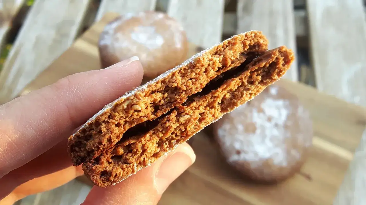 Galletas de avena crujientes, espolvoreadas con az&uacute;car glas. Una mano sostiene una galleta partida, mostrando su interior.