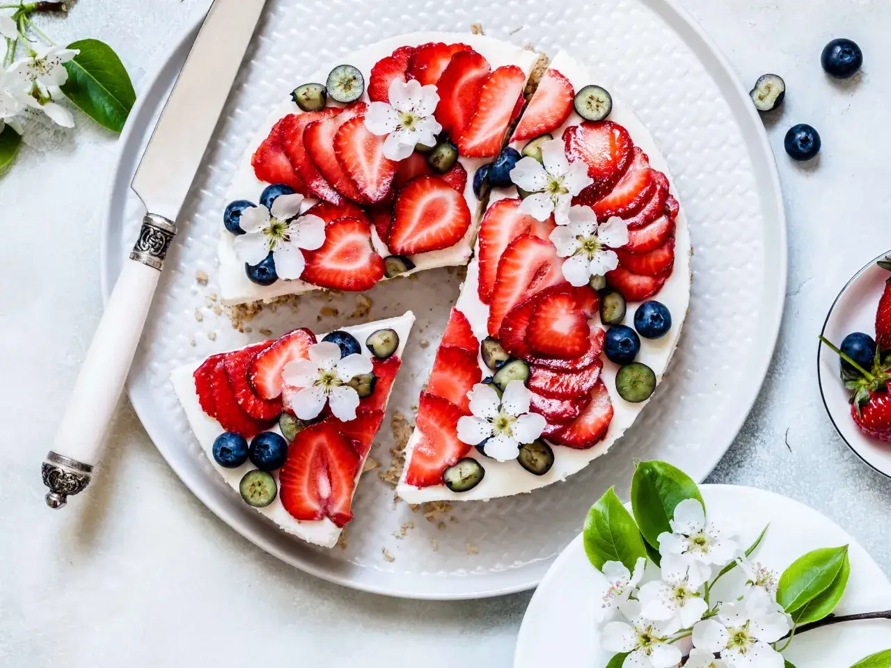 Ein köstlicher cheesecake ohne backen, dekoriert mit frischen Erdbeeren, Blaubeeren und zarten Blüten.