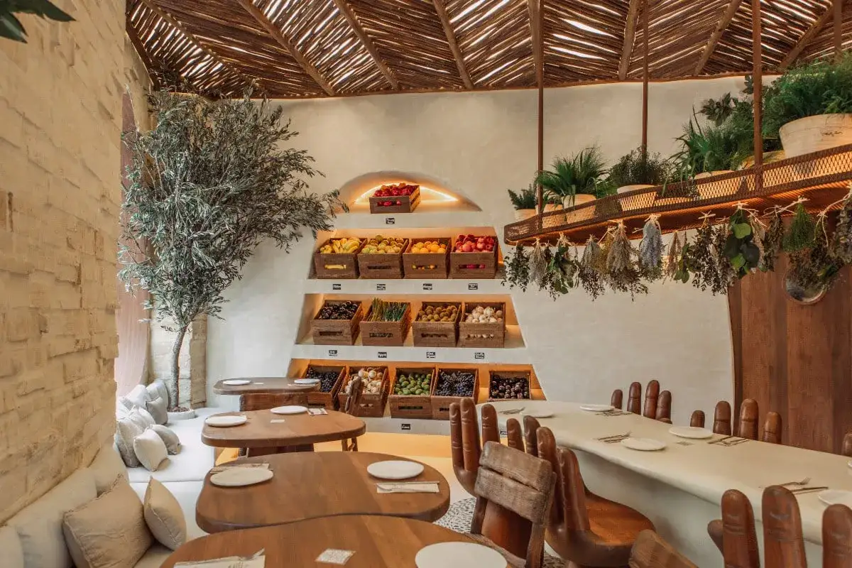 Interior de restaurantes en Valencia con encanto, con estanterías de frutas y verduras frescas, un olivo y mesas de madera.